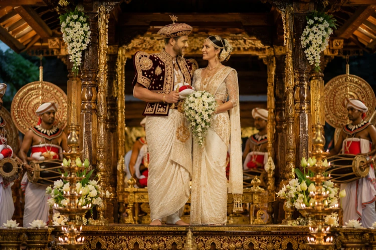 European couple dressed in traditional Kandyan wedding attire standing on a decorated poruwa during a Sri Lankan cultural wedding ceremony